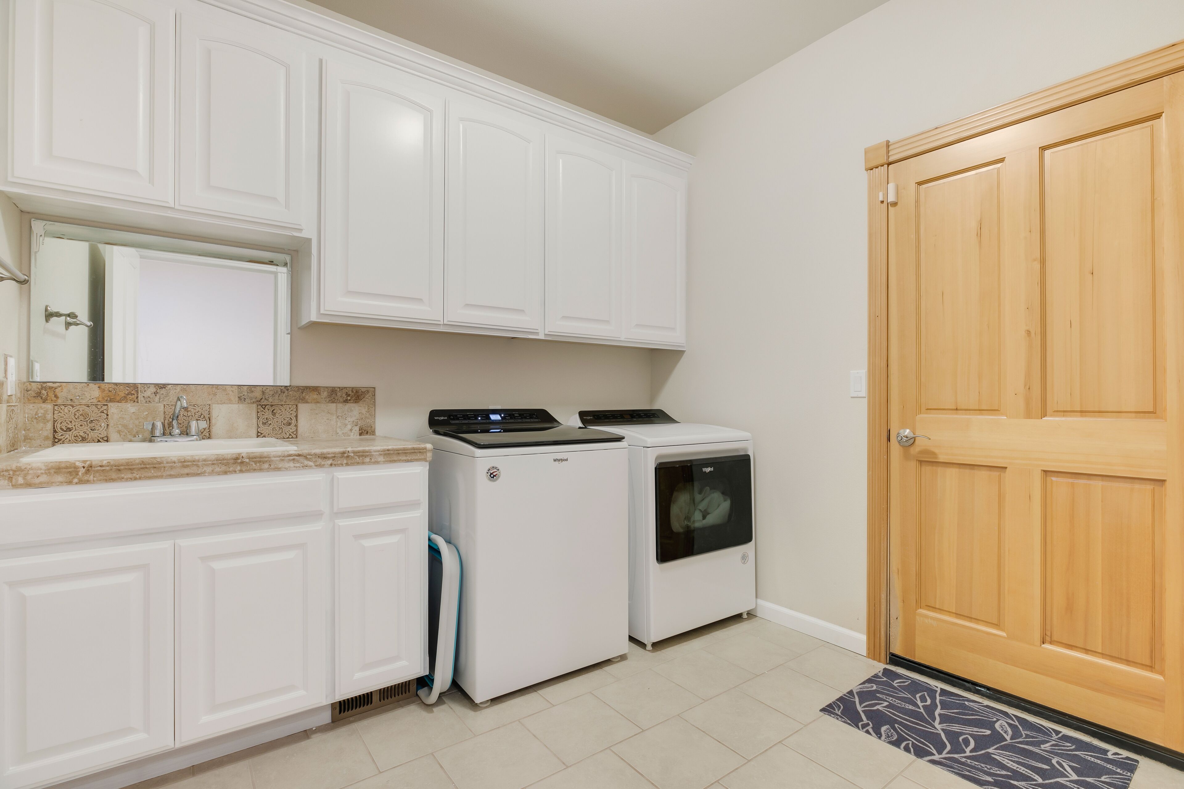 A kitchen with white cabinets, a built-in oven, a washing machine, and a wooden door.