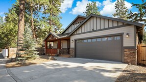 A two-story house with a garage, a covered porch, and a stone foundation. - Spacious 1 Level Sisters Home - Walk to Downtown (Sisters)