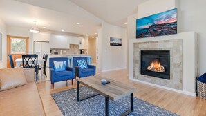A modern living room with a fireplace, blue armchairs, and a dining area in the background. - Spacious 1 Level Sisters Home - Walk to Downtown (Sisters)