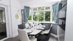 A dining area with a table set for four, a window with curtains, and a view of greenery outside. - Woodlands (Matlock)