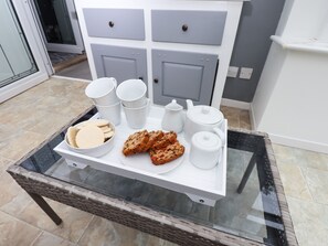 Un plateau avec des tasses blanches, une théière, un sucrier et des biscuits, le tout posé sur une table en verre.