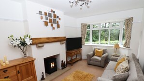 A living room with a fireplace, a sofa set, a television, and a window with curtains. - Woodlands (Matlock)