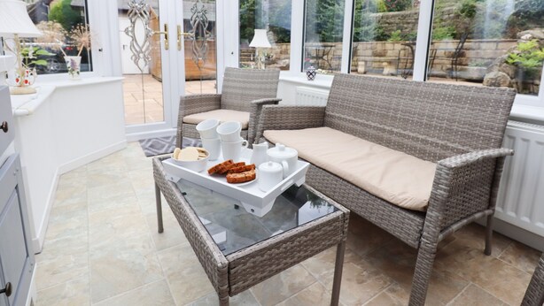 A conservatory with wicker furniture, a glass table, and a tray of food. - Woodlands (Matlock)