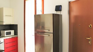 A compact kitchen with a microwave, a stainless steel refrigerator, and a wooden door. - Appartamento Stella – spazioso e moderno, vicino al centro di Bergamo (Bergamo)