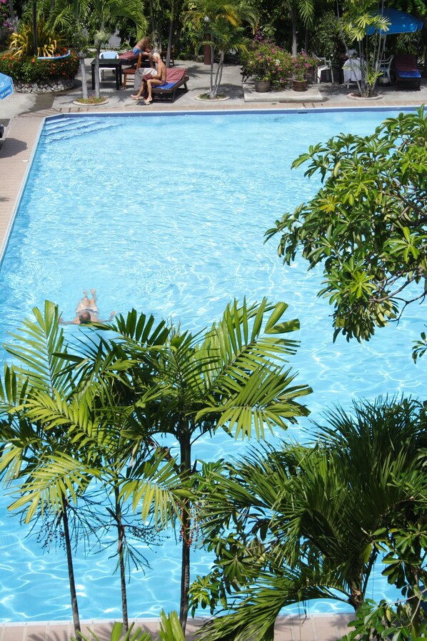 A rectangular swimming pool with clear blue water, surrounded by lush tropical foliage and outdoor seating areas. - Palm Garden Hotel (Pattaya)