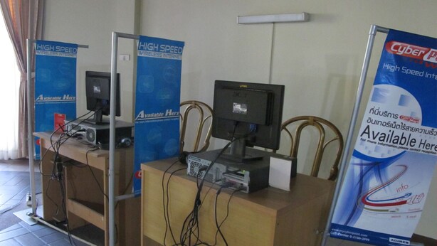 A computer station with two monitors, a keyboard, and a mouse. There are posters on the wall advertising high-speed wireless internet. - Palm Garden Hotel (Pattaya)