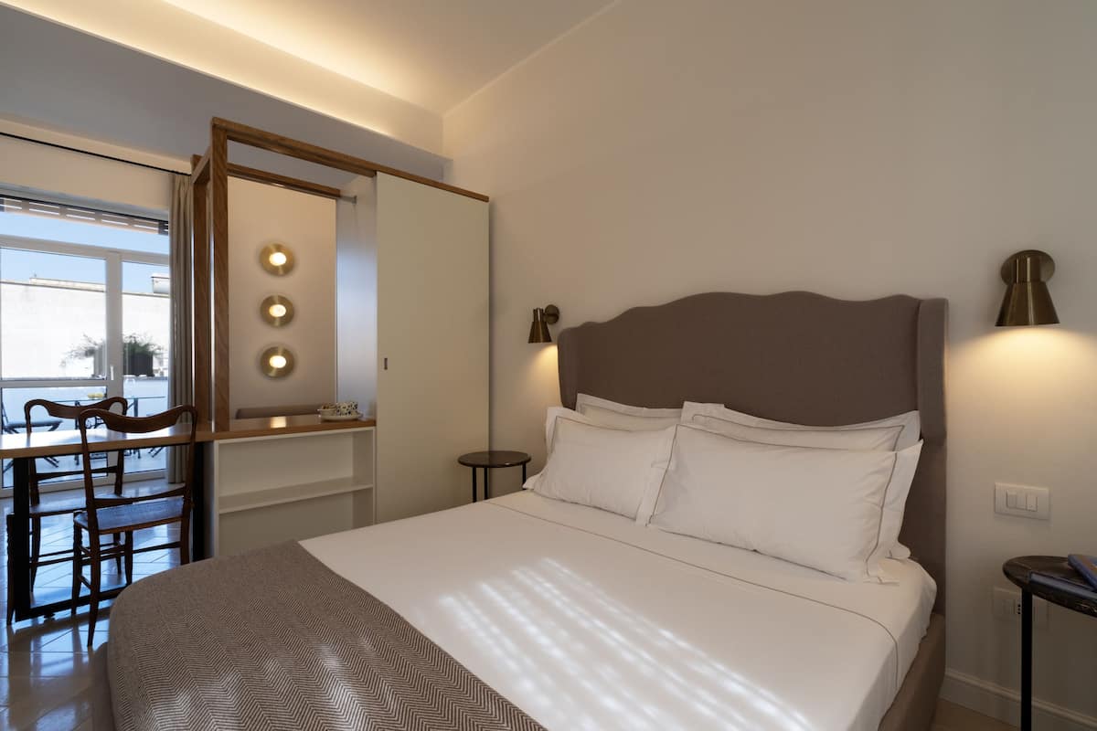 Un dormitorio con una cama grande, un escritorio con silla, un espejo y una lámpara de pared.