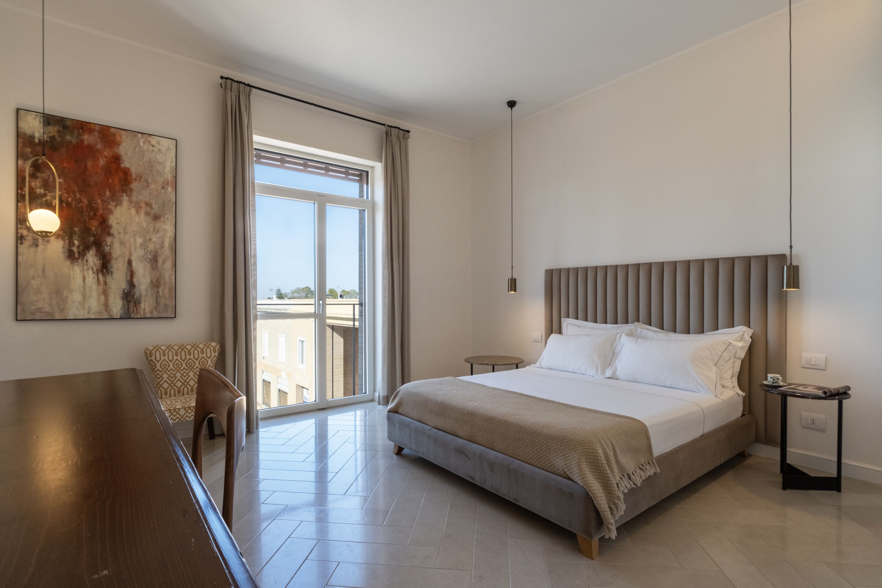 A modern hotel room with a large bed, a dining table, and a view of the outdoors.