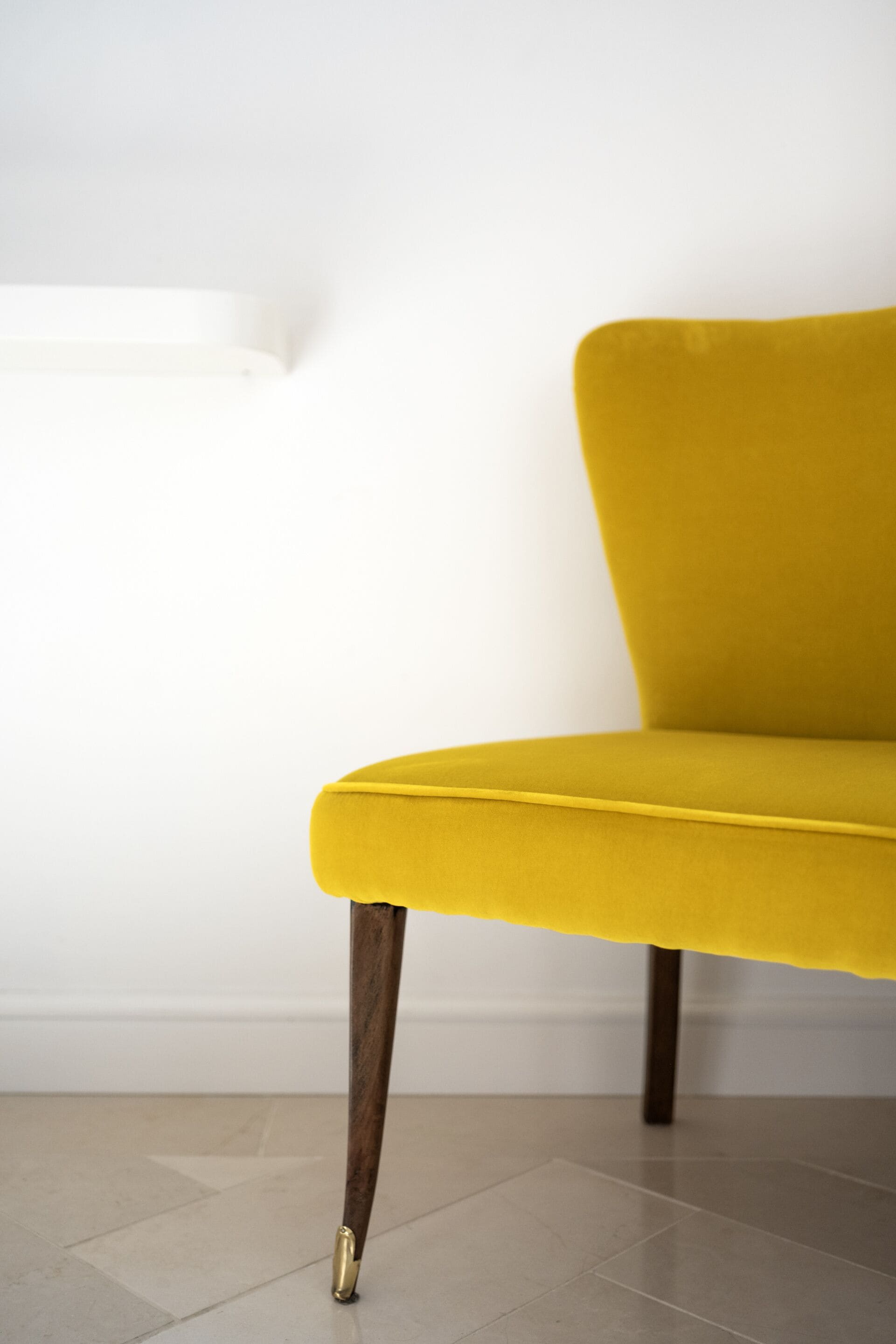 A yellow chair with wooden legs against a white wall.