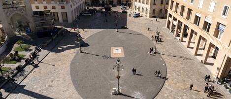 An open square with a central monument, surrounded by historic buildings with balconies and arches.