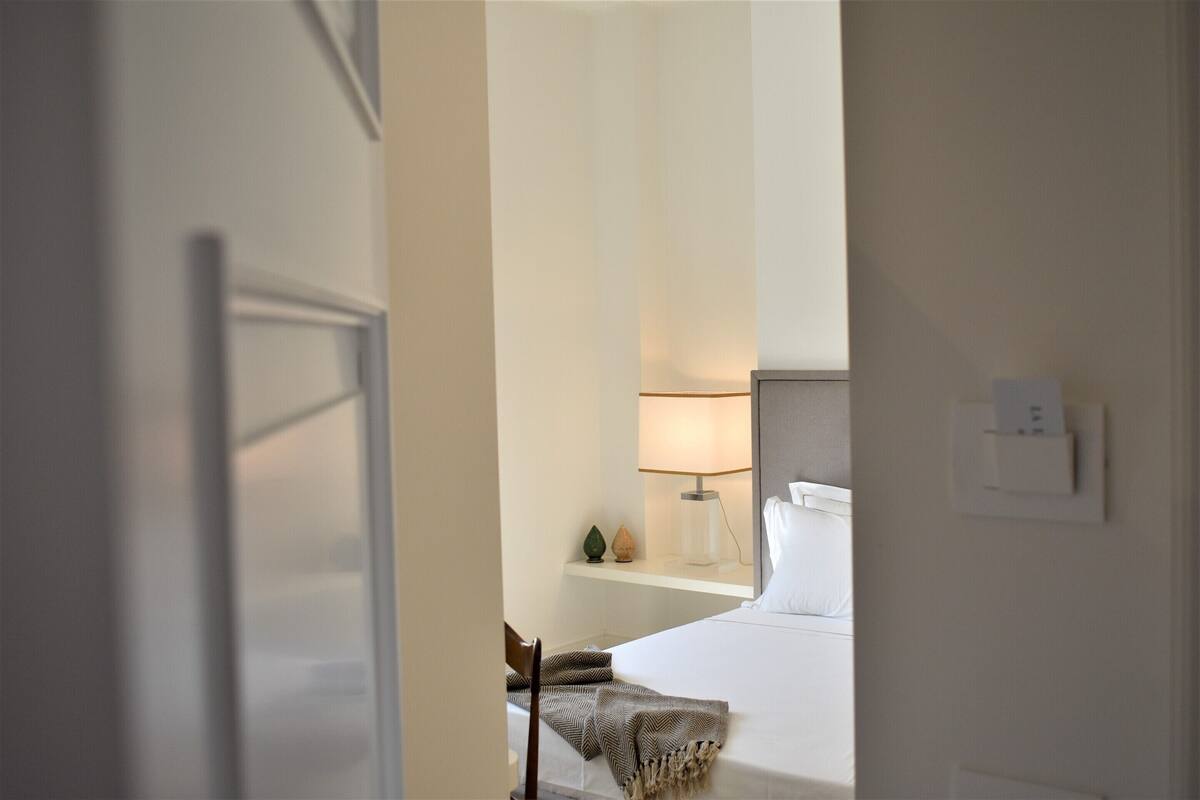 Una habitación de hotel con una cama, una lámpara de noche, un estante con adornos y una silla.