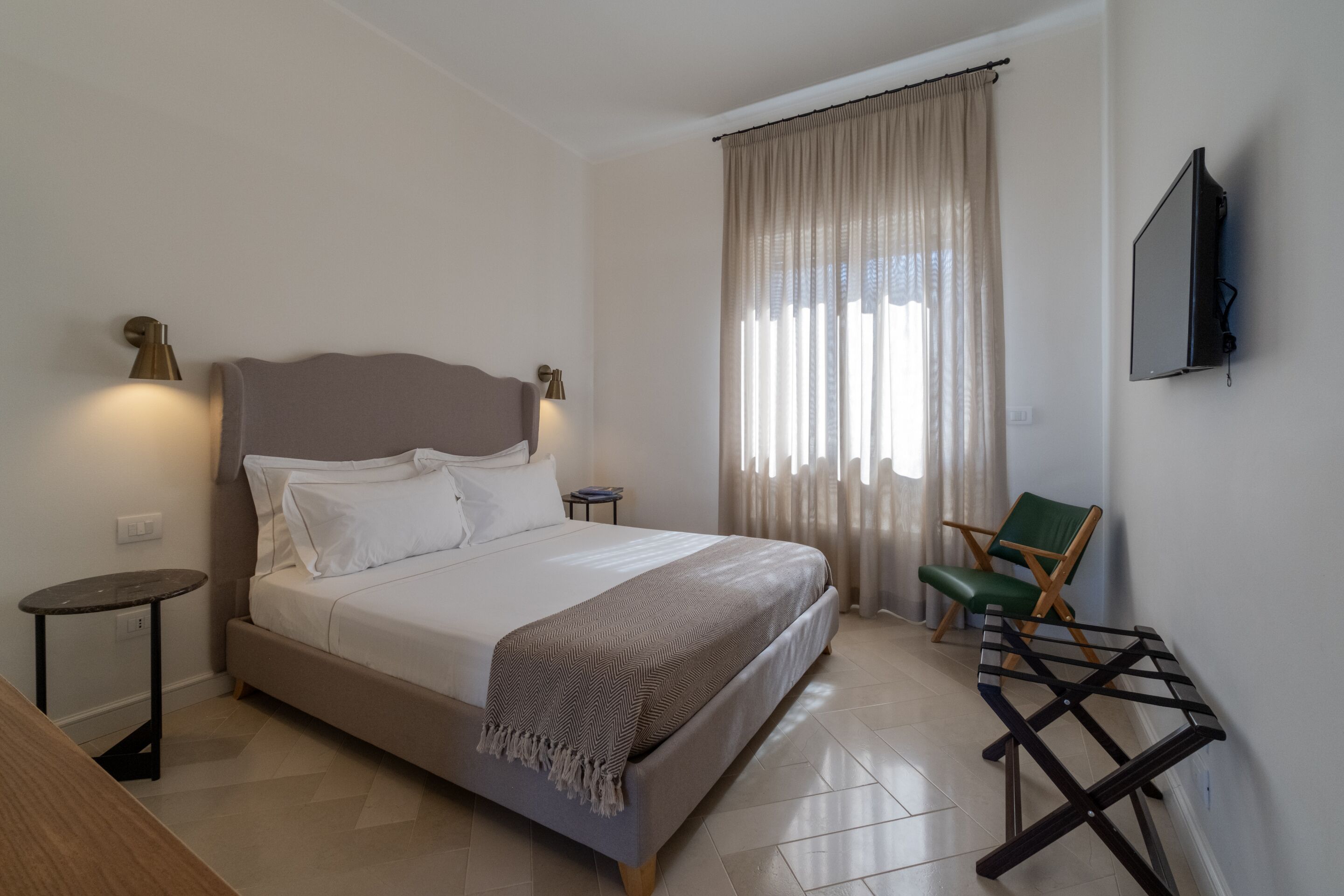 A neatly arranged bedroom with a bed, bedside tables, a chair, and a TV mounted on the wall.