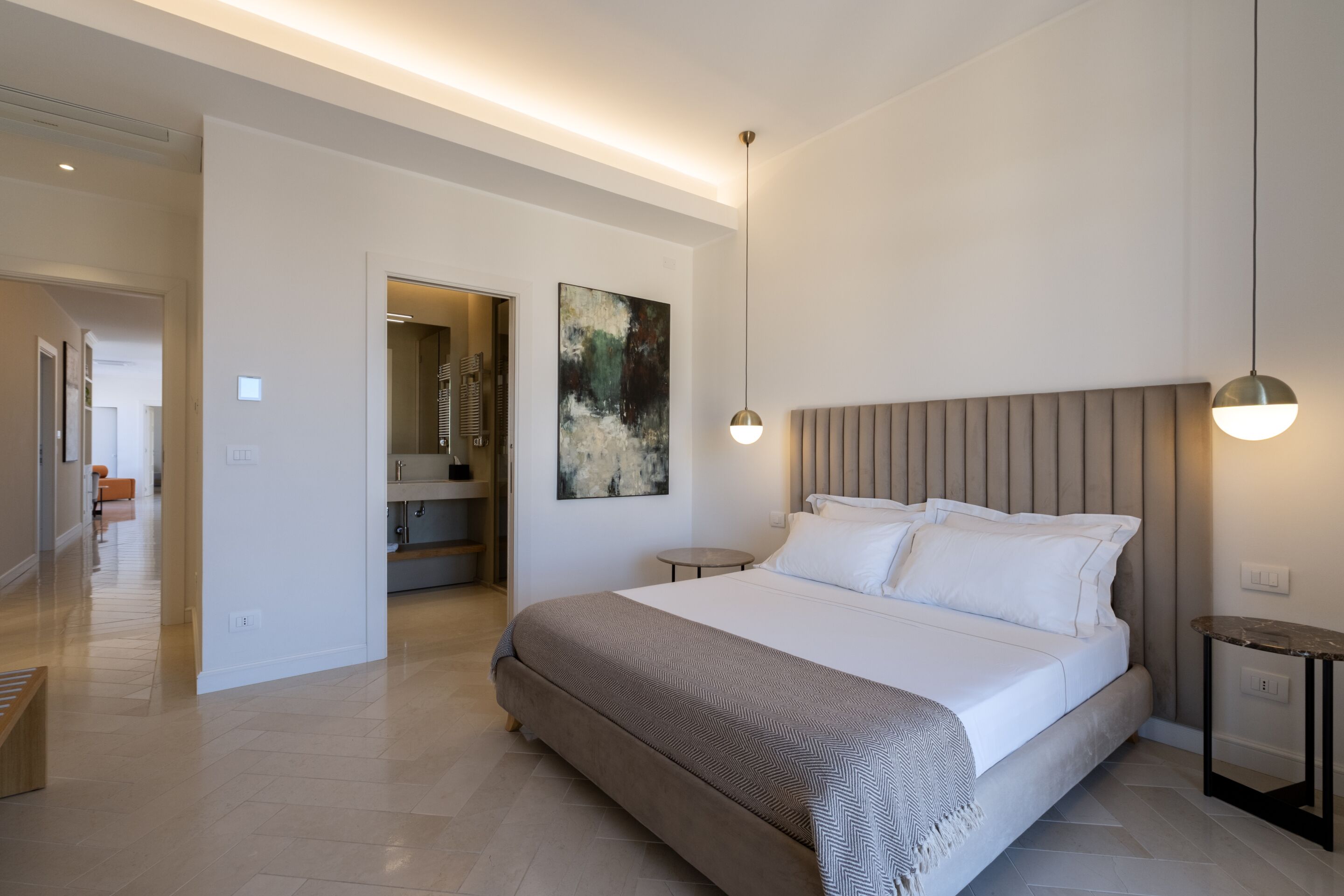 A modern bedroom with a large bed, a bedside table, a hanging light, and a painting on the wall.