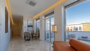 A modern living room with a sofa, chairs, a table, and a large window offering a view of the city. - Abalto Suites & Rooms (Lecce)