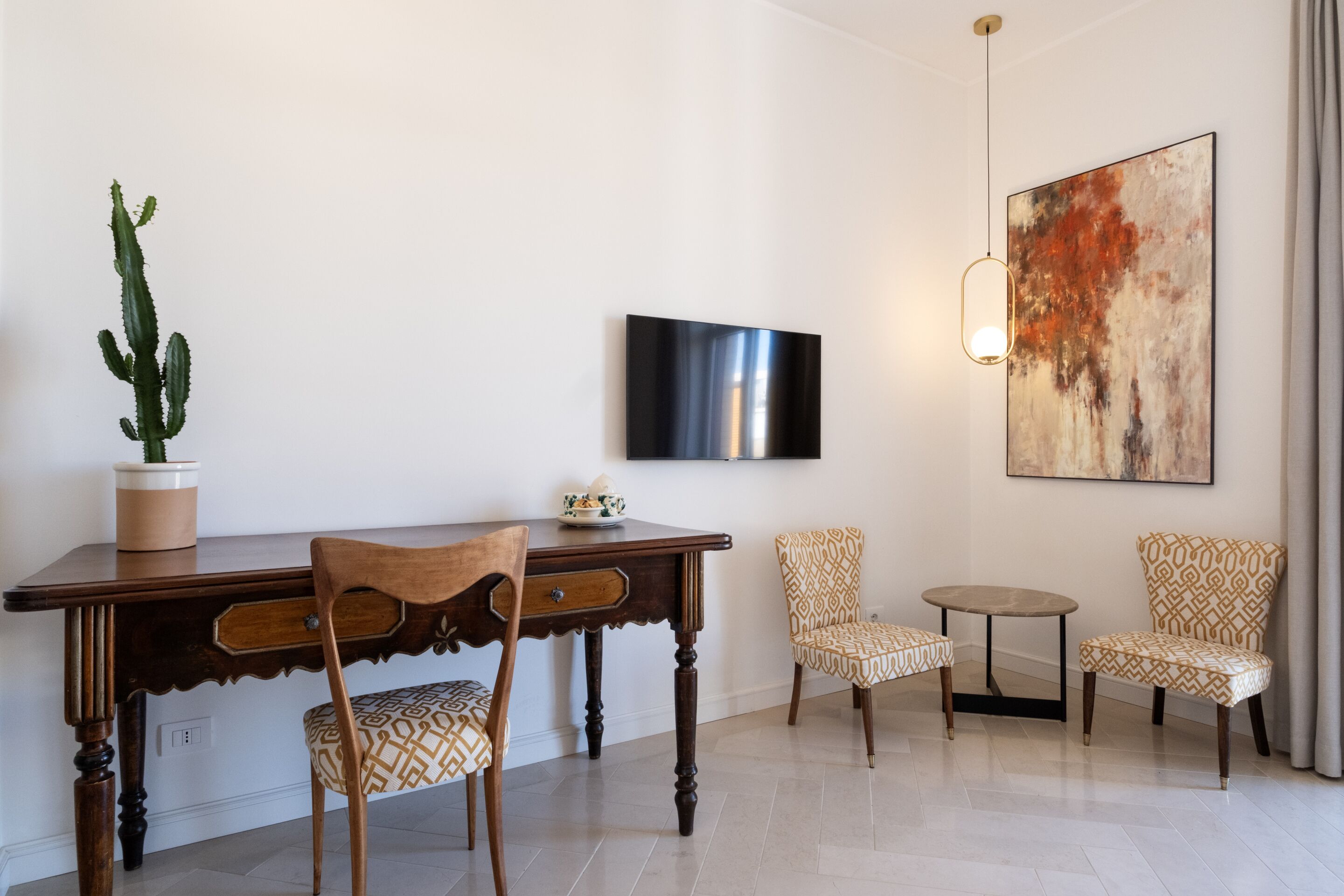 Una sala moderna con una mesa de comedor de madera, dos sillas estampadas, una mesita redonda pequeña, una planta de cactus, un televisor de pantalla plana y un cuadro abstracto grande en la pared.