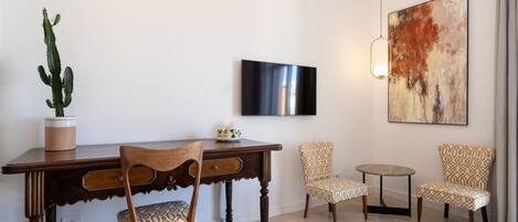 Una sala moderna con una mesa de comedor de madera, dos sillas estampadas, una mesita redonda pequeña, una planta de cactus, un televisor de pantalla plana y un cuadro abstracto grande en la pared.
