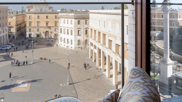 A room with a large window overlooking a historic square with buildings and a statue. - Abalto Suites & Rooms (Lecce)