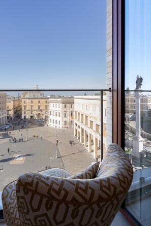 Una habitación con un amplio ventanal que da a una plaza histórica con edificios y una estatua.
