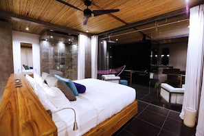 A modern bedroom with a wooden bed, a glass-enclosed balcony, and a stone wall shower. - Kura Design Villas (Ballena)
