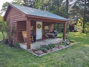 A log cabin with a porch, a dining table, and a grill.