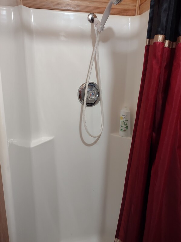 A shower with a handheld showerhead, a bottle of Dove body wash, and a red curtain.