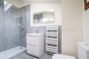 A modern bathroom with a glass shower enclosure, a white vanity with a mirror, and a towel rack. - The Pigsty - sleeps 2 guests in 1 bedroom (York)