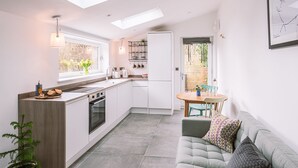 A modern kitchen with skylights, a dining area with a table and chairs, and a sofa with cushions. - The Pigsty - sleeps 2 guests  in 1 bedroom (York)