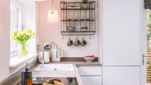 A modern kitchen with white cabinetry, a built-in oven, a coffee machine, and a shelf with kitchenware. - The Pigsty - sleeps 2 guests  in 1 bedroom (York)