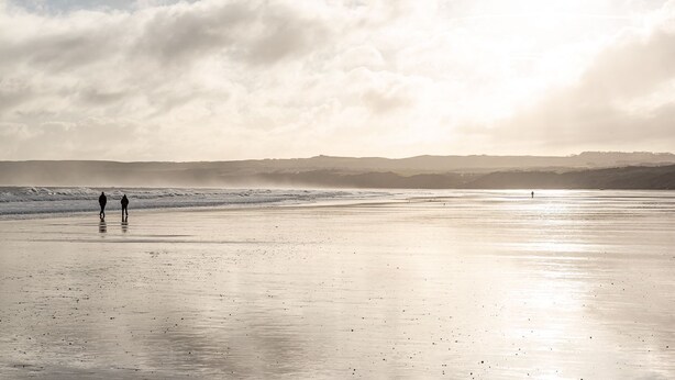 A beach with two people walking, a calm sea, and a cloudy sky. - The Pigsty - sleeps 2 guests  in 1 bedroom (York)