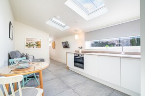 A modern kitchen with a skylight, a dining area with a table and chairs, and a view through the window.