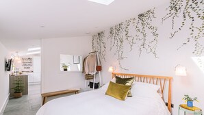 A bedroom with a bed, bedside tables, a hanging plant, and a view into the kitchen. - The Pigsty - sleeps 2 guests  in 1 bedroom (York)