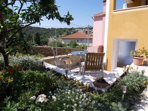 Een terras met een tafel en stoelen, omringd door een tuin met verschillende planten en bloemen.