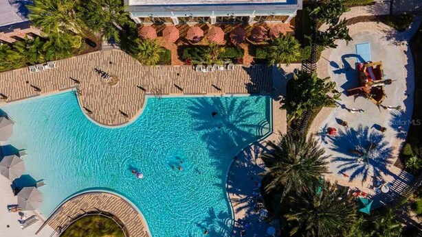 Eine Vogelperspektive zeigt einen luxuriösen Resortkomplex mit einem großen Pool, der von Palmen, Liegestühlen und Sonnenschirmen umgeben ist.