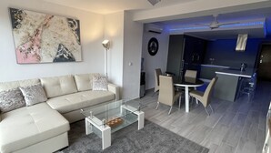 Un salon moderne avec une table basse en verre, un canapé et un coin repas avec des chaises.