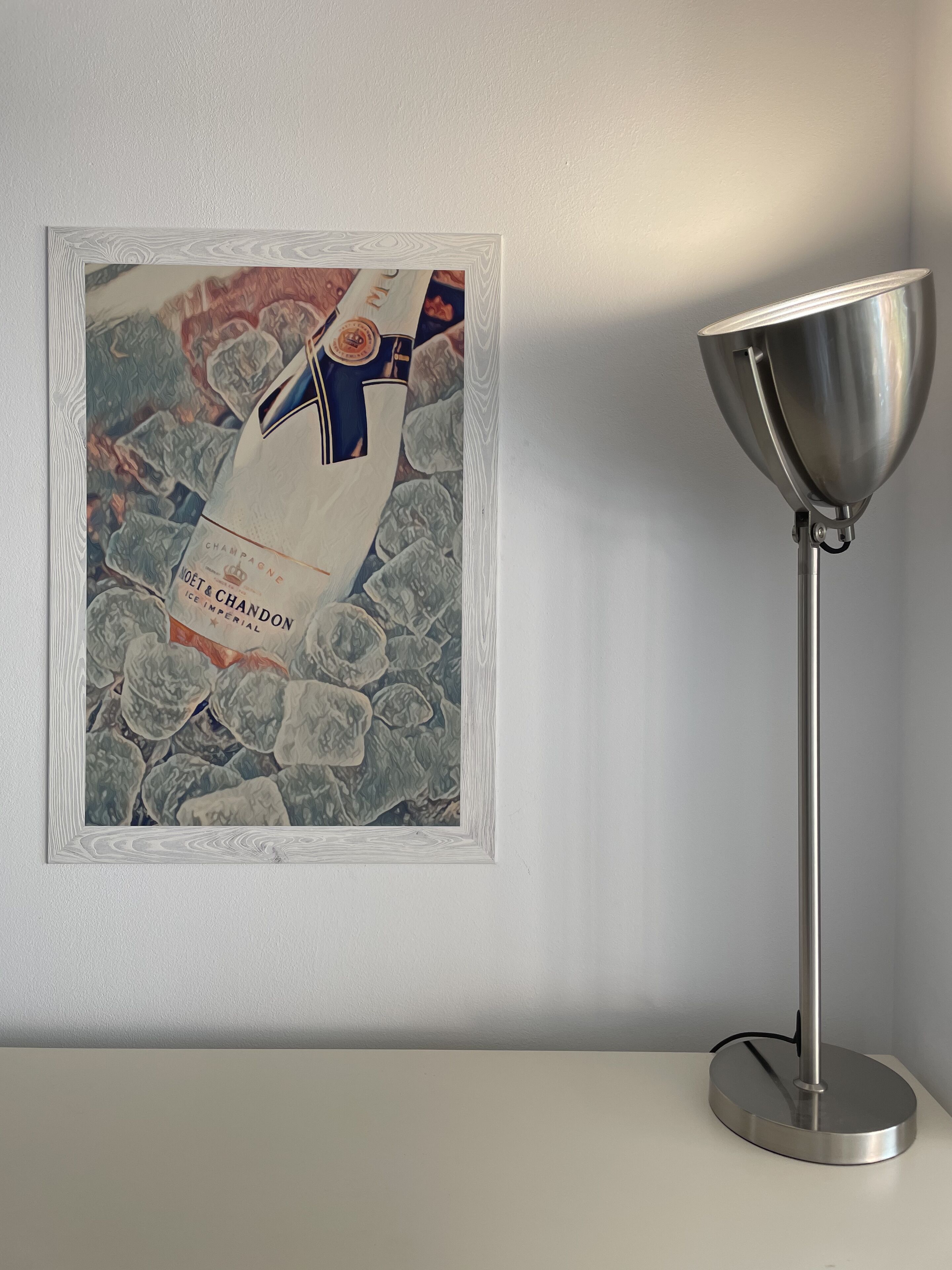 A framed artwork of a champagne bottle on a wall, next to a modern floor lamp.