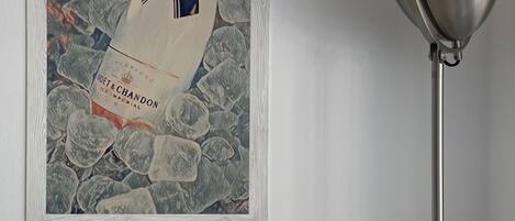A framed artwork of a champagne bottle on a wall, next to a modern floor lamp.