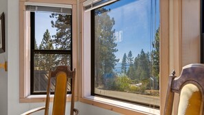 A room with a wooden chair and a window with a view of trees and a house.