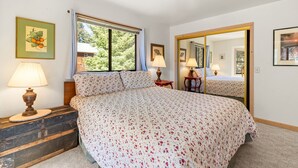 A bedroom with a large bed, two bedside lamps, a dresser, a window with curtains, and a mirror.