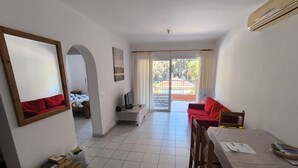 Un vaste espace de vie comprenant un canapé rouge, une table à manger en bois et un téléviseur posé sur un meuble.