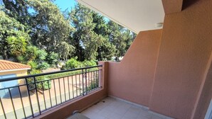 Un balcon avec deux chaises, une rambarde en métal et une vue sur des arbres et un immeuble.