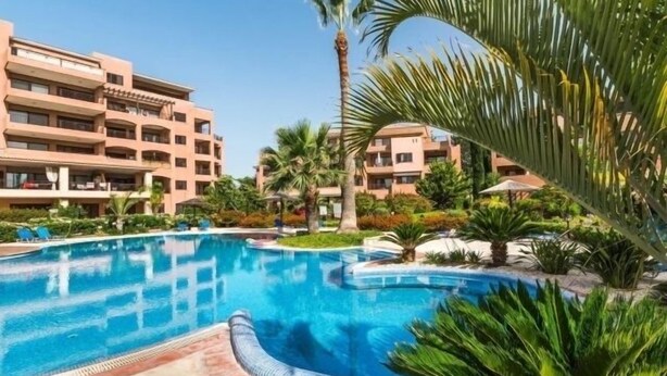 Une piscine entourée de palmiers et un immeuble à plusieurs étages doté de balcons.
