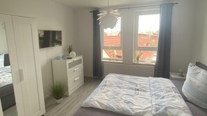 Une chambre à coucher avec un lit, une commode, un miroir et une fenêtre avec des rideaux.
