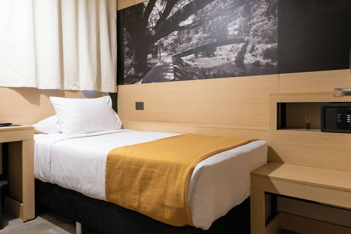 A hotel room with a bed, a nightstand, a desk, and a wall-mounted TV.