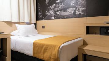 Quarto de hotel com cama, mesa de cabeceira, escrivaninha e televisão presa à parede.