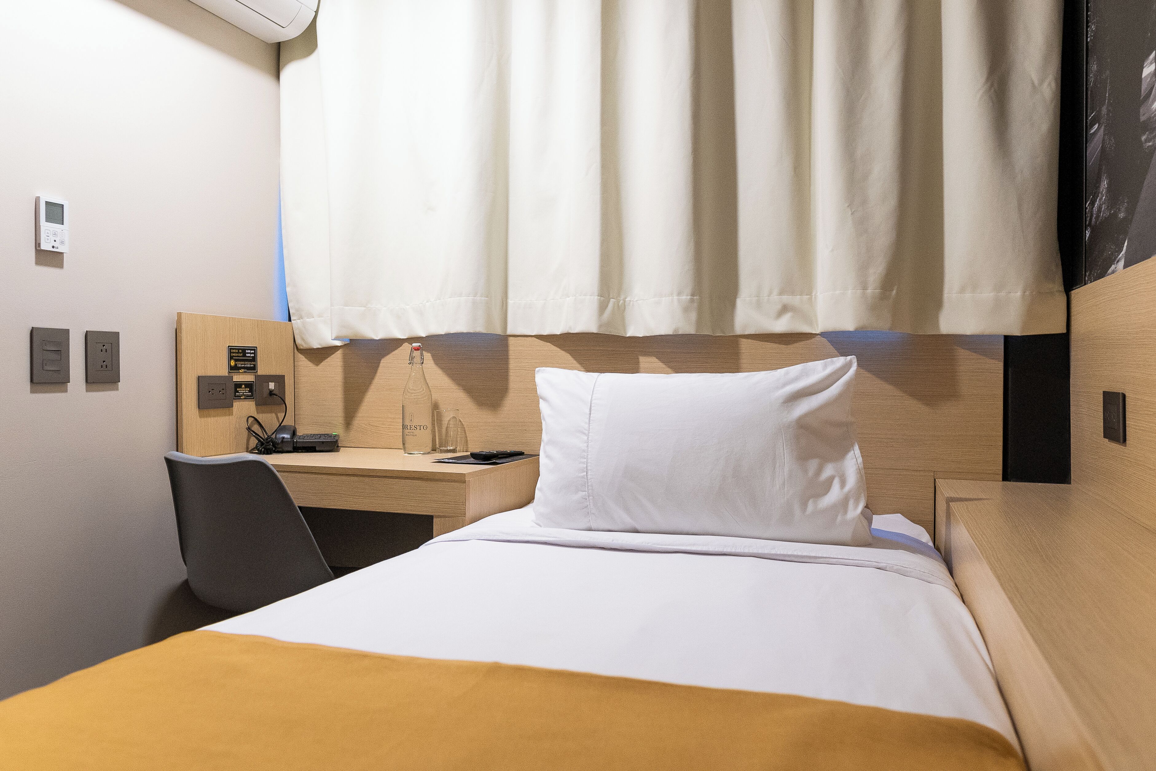 Une chambre d’hôtel avec un lit, un bureau, une chaise et une fenêtre avec des rideaux.