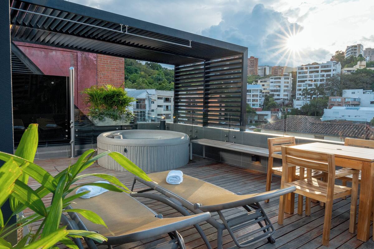 A rooftop terrace with a hot tub, lounge chairs, and a wooden table.