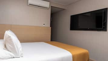 A hotel room with a bed, a television mounted on the wall, and an air conditioning unit above the bed.