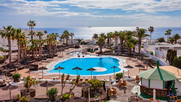 Un espace piscine d’un complexe hôtelier offrant une vue dégagée sur l’océan, entouré de palmiers et de chaises longues.