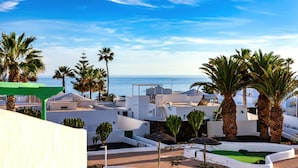 Un complexe hôtelier avec des bâtiments blancs, des palmiers et une vue sur la mer.