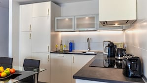 Une cuisine moderne avec des meubles blancs, un plan de travail noir et un coin repas doté d’une table en verre.